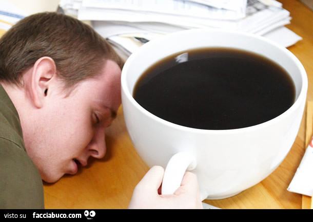 Addormentato sulla scrivania vicino a tazza enorme di caffè