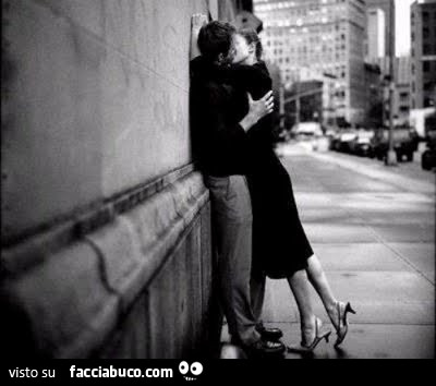 Bacio appassionato tra uomo e donna sul marciapiede contro il muro